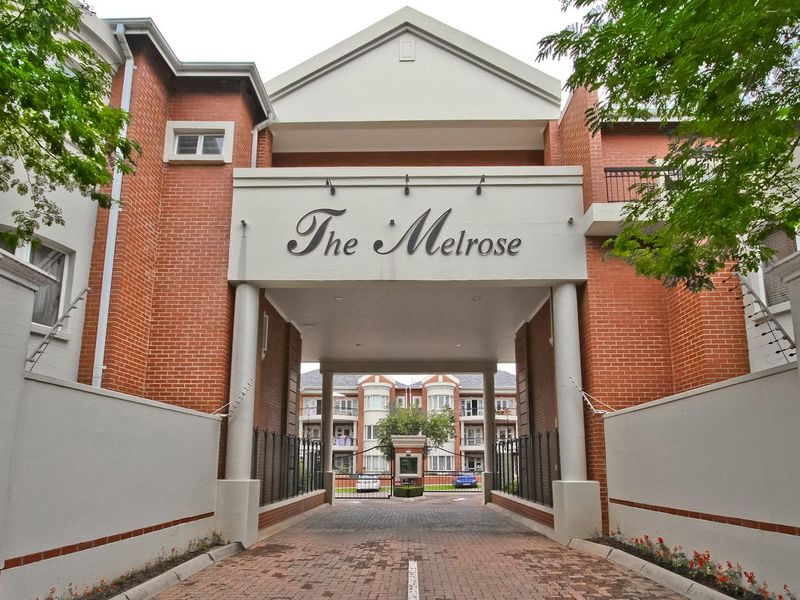 The front entrance of The Melrose apartment complex, featuring a secure gated driveway, brick facade, and well-maintained architectural detailing.