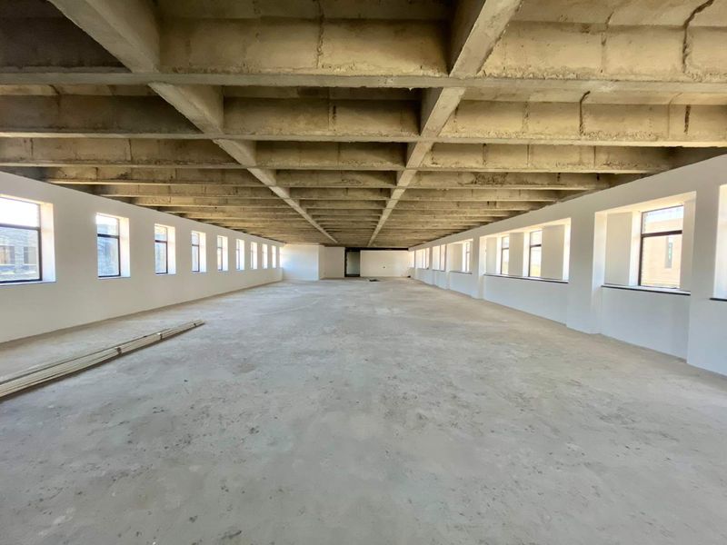 A large, open-plan office space in shell condition featuring an exposed concrete waffle ceiling, concrete flooring, and abundant natural light from multiple windows.