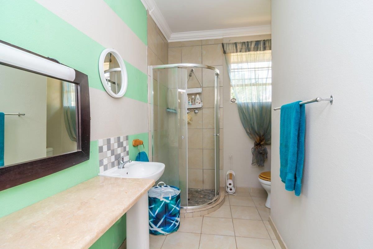 A functional bathroom featuring a corner shower enclosure, pedestal basin with stone countertop, and tiled flooring.