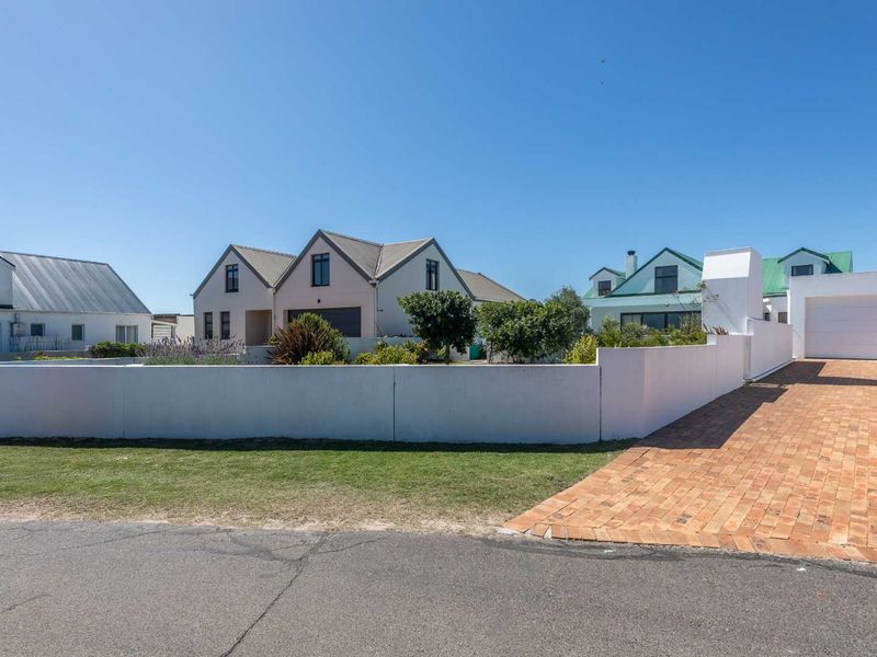 Front view of the property featuring a brick driveway, white boundary wall, and garage access.