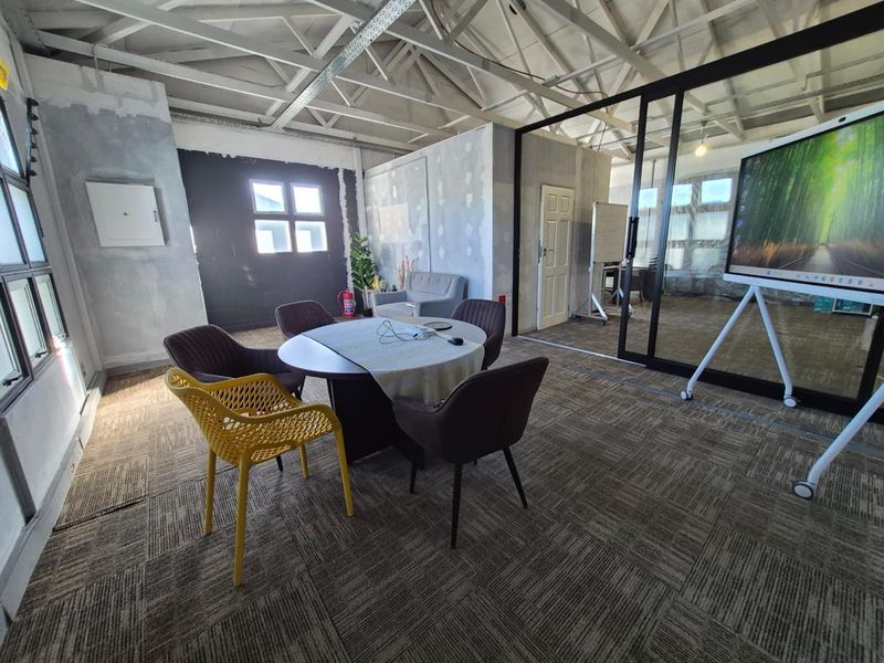 An office space featuring exposed roof trusses, carpet tiles, and a modern glass partition wall, currently requiring finishing touches to the wall surfaces.