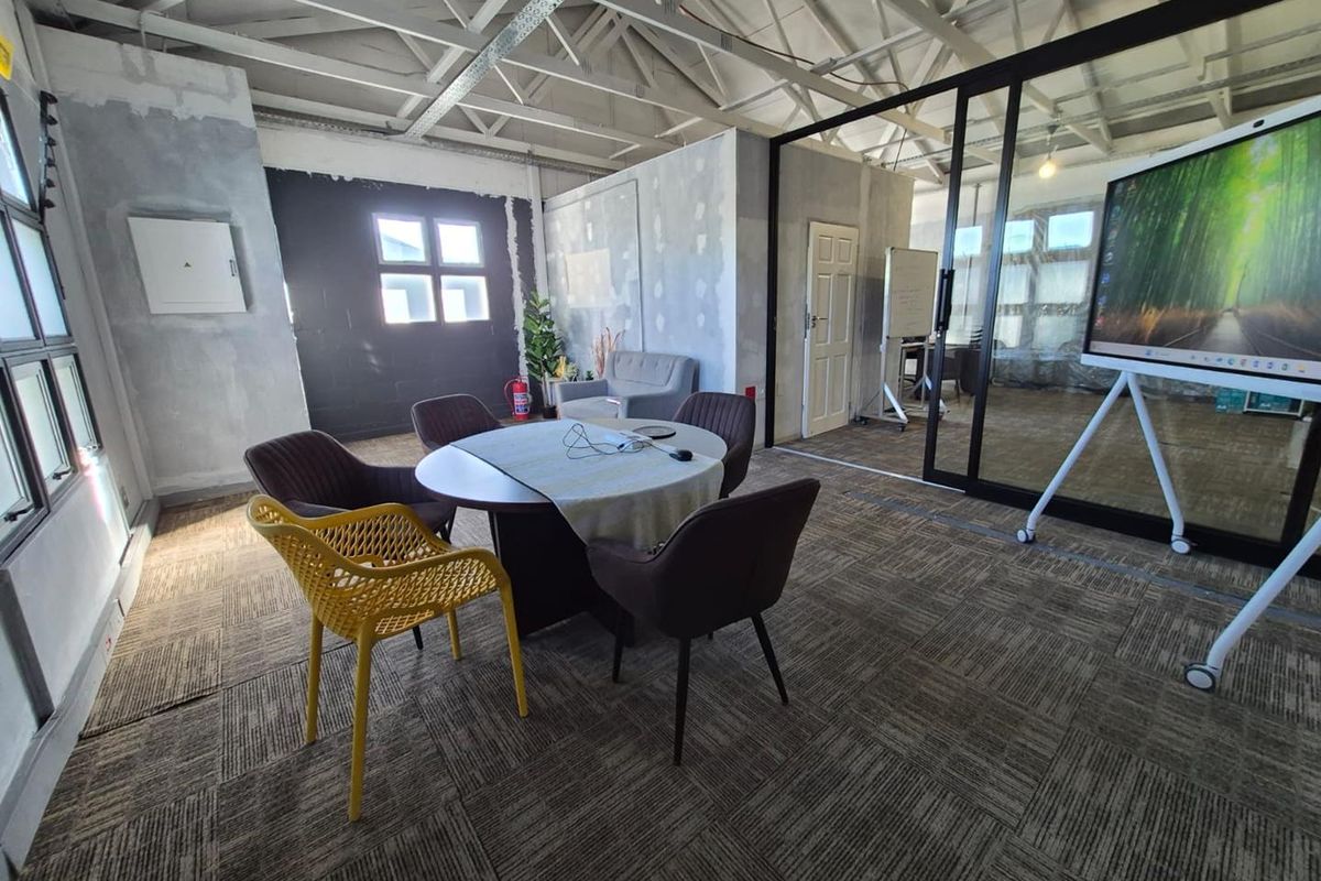 An office space featuring exposed roof trusses, carpet tiles, and a modern glass partition wall, currently requiring finishing touches to the wall surfaces.