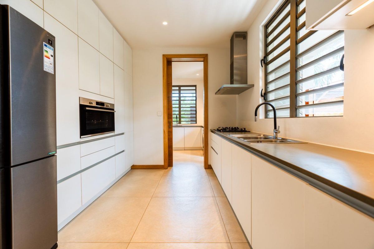 Modern galley-style kitchen featuring sleek white cabinetry, stone countertops, stainless steel built-in oven, extractor fan, and a double sink with a contemporary faucet.