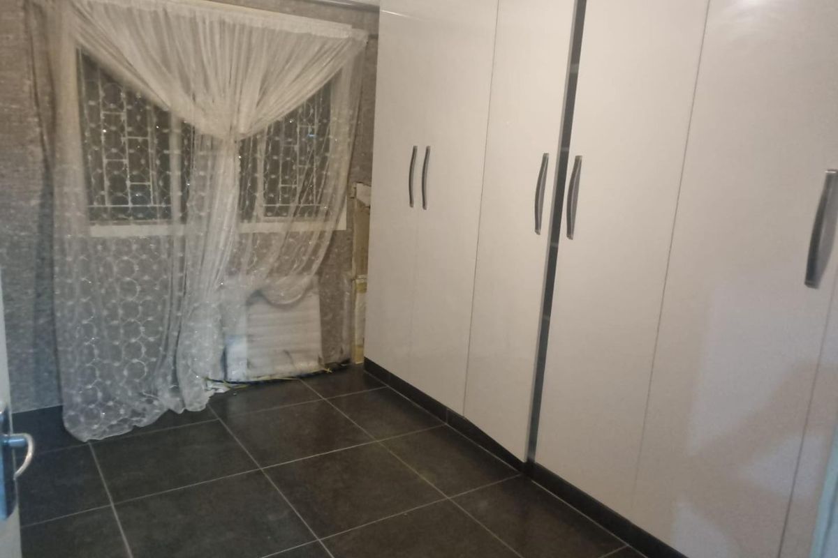 A bedroom featuring modern white built-in cupboards and dark tiled flooring, providing a clean and functional storage space.