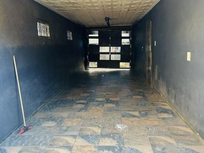A spacious, empty garage featuring tiled flooring, a textured ceiling, and a secure metal garage door, providing ample storage or parking space.