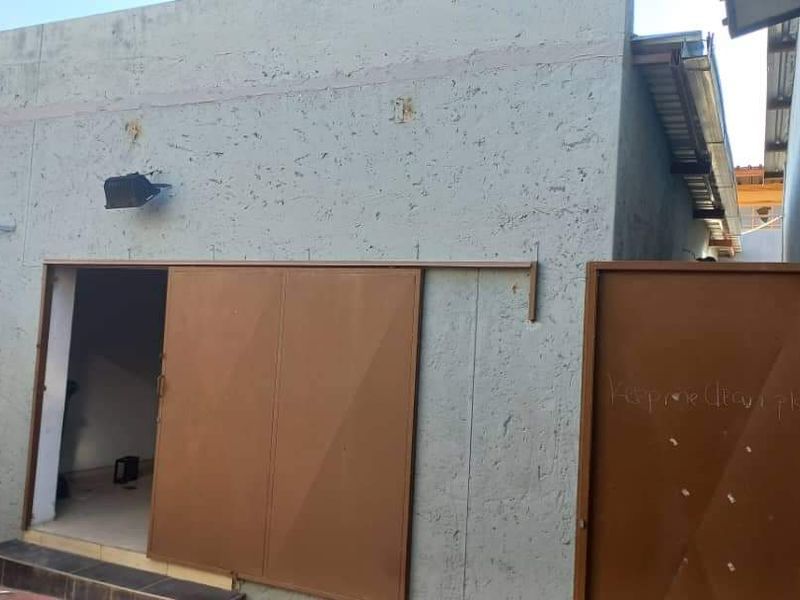 Rear exterior view of an industrial building featuring a sliding metal door, pedestrian access, and textured wall finish with visible surface wear.