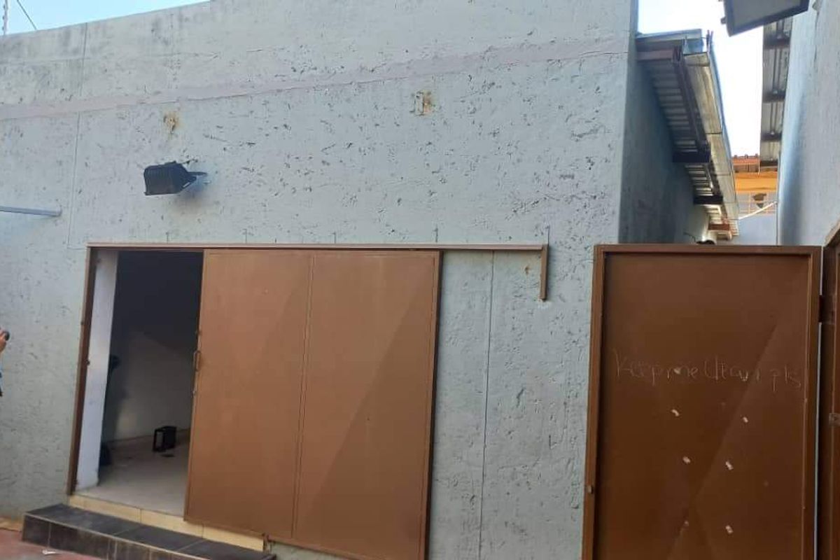 Rear exterior view of an industrial building featuring a sliding metal door, pedestrian access, and textured wall finish with visible surface wear.