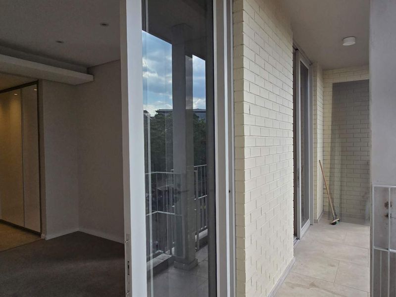 A spacious covered balcony featuring tiled flooring, a modern metal balustrade, and large sliding glass doors leading into the interior living space.