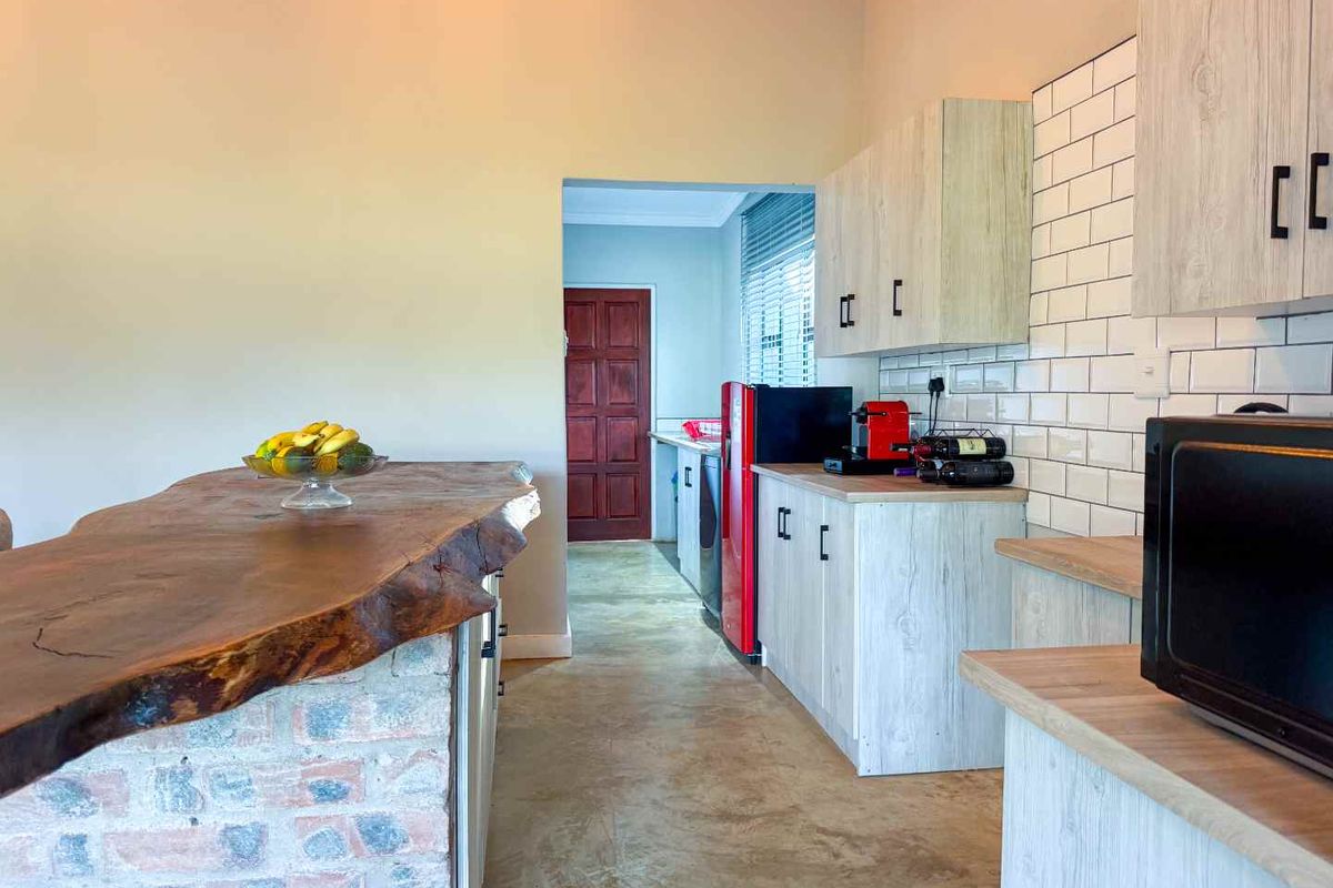 A rustic-style kitchen featuring a live-edge timber breakfast bar, exposed brick base, subway tile backsplash, and light wood-grain cabinetry.