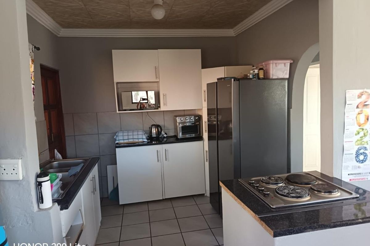 A functional kitchen featuring white cabinetry, granite countertops, a built-in electric hob, and tiled flooring, offering a practical layout for daily meal preparation.