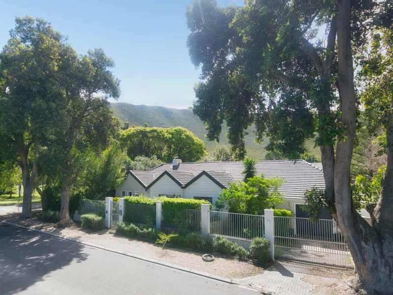 Front elevation of a residential property featuring a tiled roof, secure metal perimeter fencing, and mature trees set against a mountain backdrop.