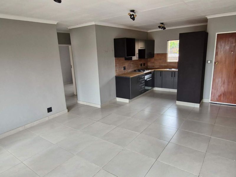 An open-plan living and kitchen area featuring tiled flooring, modern dark cabinetry, and built-in cooking appliances in a neutral, well-maintained space.