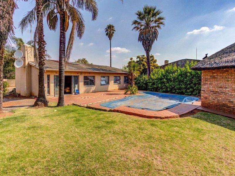 Rear garden view featuring a swimming pool with cover, paved patio area, and a secondary structure with a traditional thatched roof.
