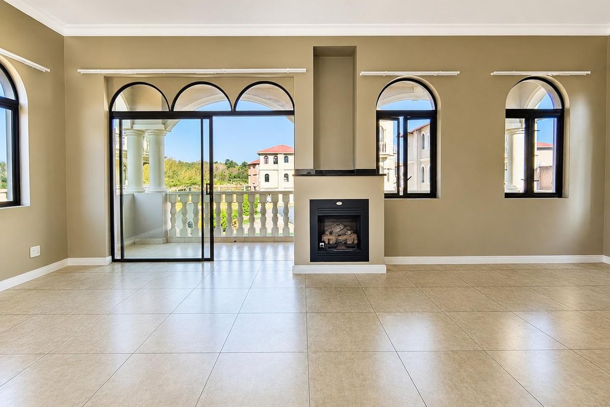 Spacious living room featuring neutral tiled flooring, a built-in fireplace, and large arched windows with access to a private balcony.