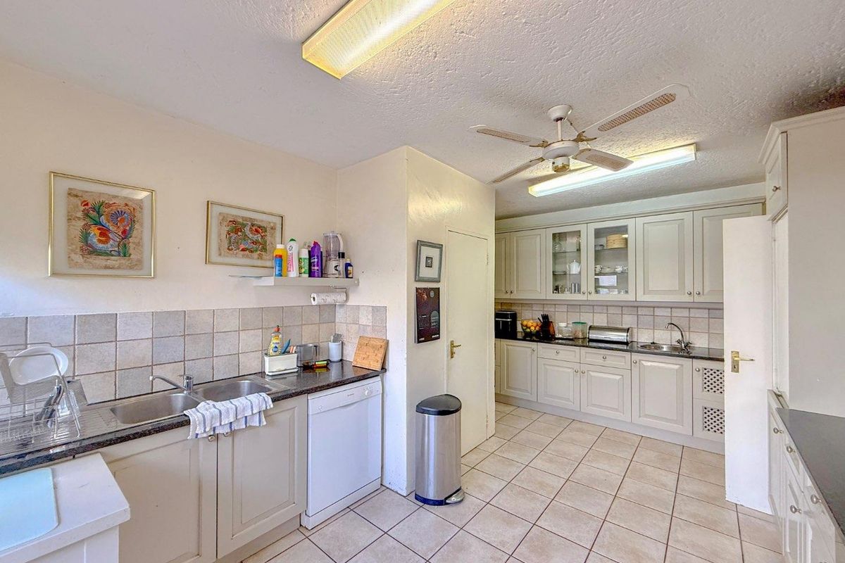 A functional kitchen featuring neutral cabinetry, tiled splashbacks, double stainless steel sink, and tiled flooring with ample storage space.