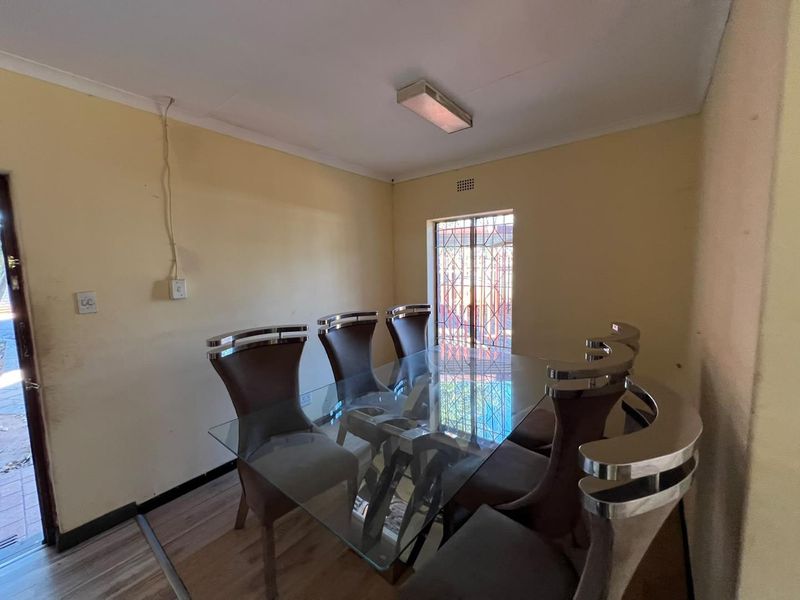 Dining room featuring laminate flooring, a security gate on the window, and surface-mounted lighting, requiring cosmetic updates to the walls and electrical finishes.