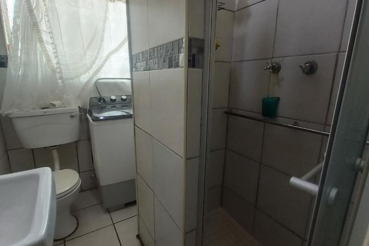 A dated bathroom featuring a shower enclosure, toilet, and wash basin with visible wear to the tiled surfaces and ceiling.