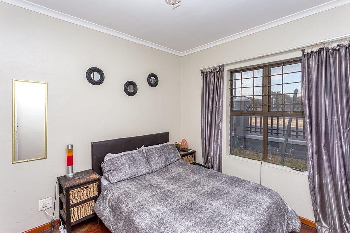 A bedroom featuring wooden flooring, cove cornicing, and a window fitted with security burglar bars.
