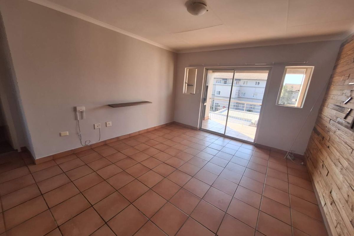 An empty living room featuring tiled flooring, a timber accent wall, and a sliding glass door providing access to a balcony.