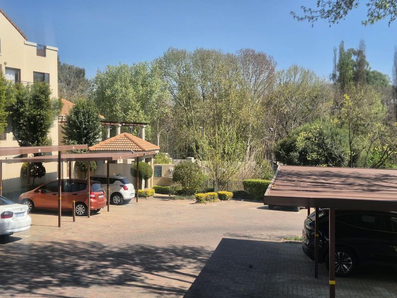Exterior view of the apartment complex parking area featuring covered carports and paved driveway with surrounding landscaped garden.