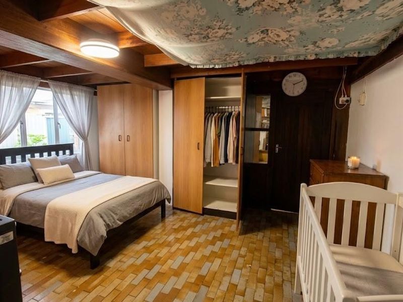 A bedroom featuring exposed timber ceiling beams, built-in wooden wardrobes, and tiled flooring, offering a rustic aesthetic with functional storage space.