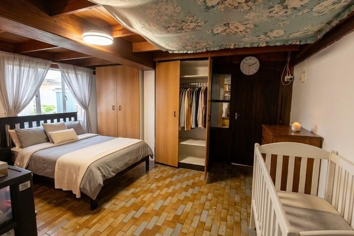 A bedroom featuring exposed timber ceiling beams, built-in wooden wardrobes, and tiled flooring, offering a rustic aesthetic with functional storage space.