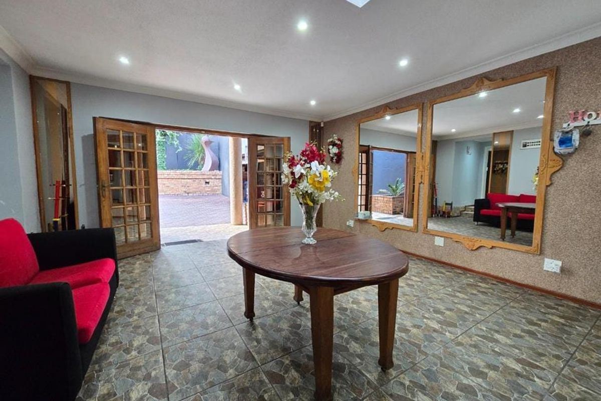 Spacious living area featuring tiled flooring, recessed downlights, a skylight, and large wall-mounted mirrors, with direct access to an outdoor patio through timber french doors.