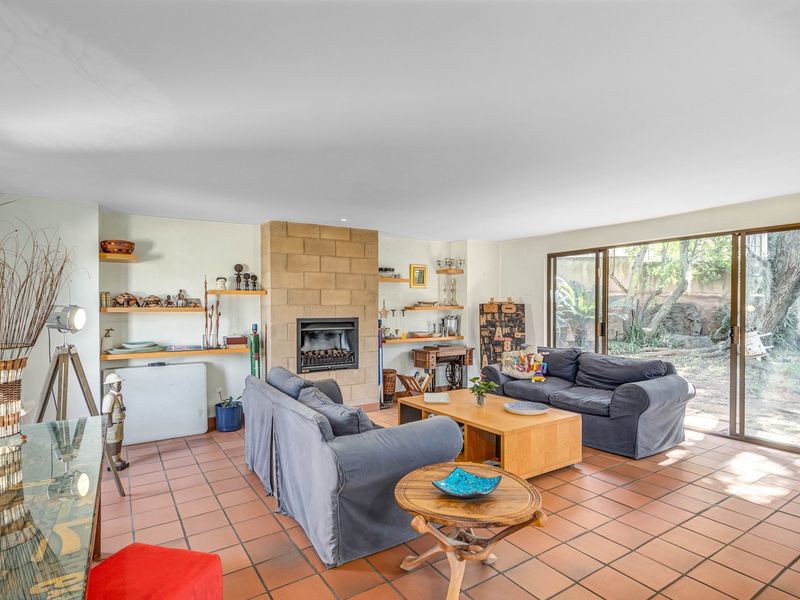 Spacious living room featuring a stone fireplace, built-in shelving, terracotta tile flooring, and large sliding glass doors providing access to the garden.