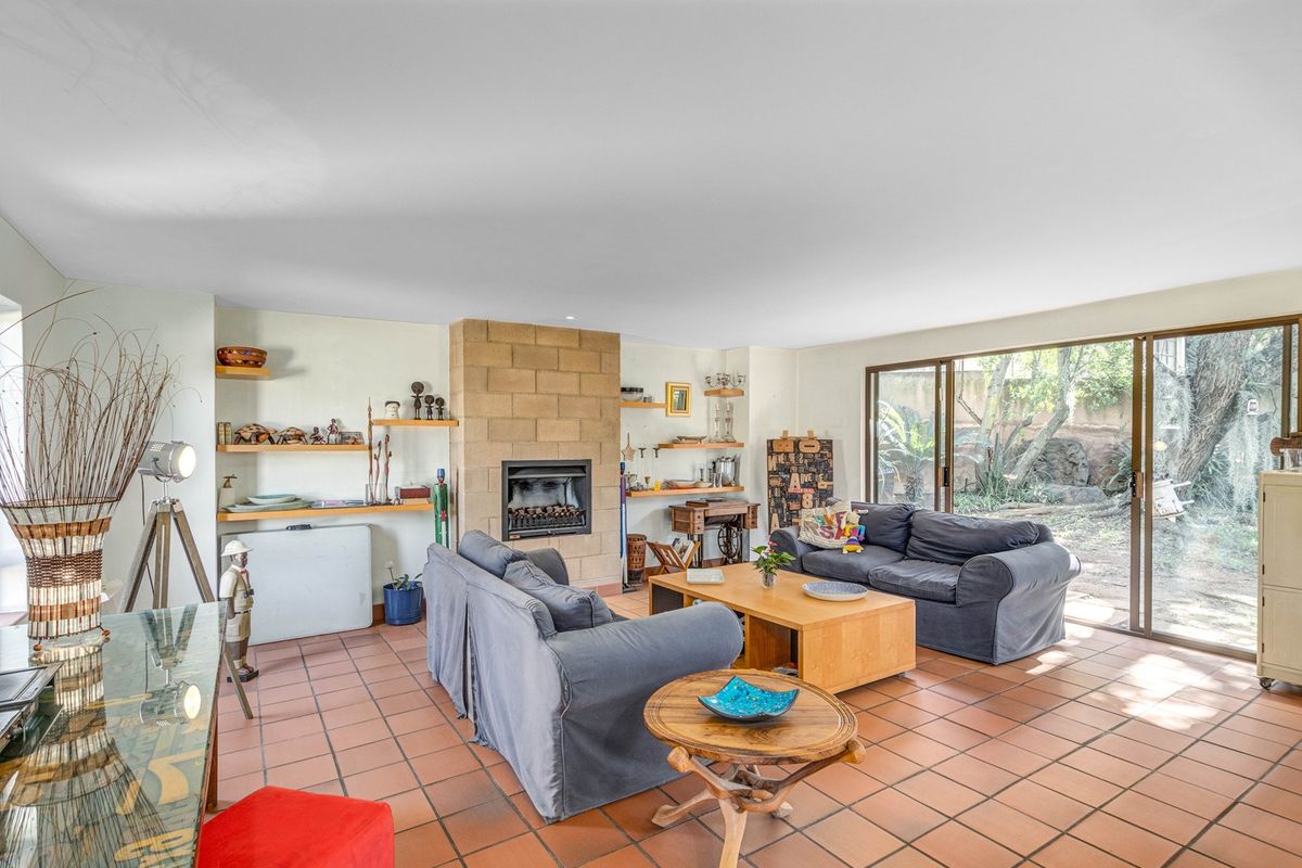 Spacious living room featuring a stone fireplace, built-in shelving, terracotta tile flooring, and large sliding glass doors providing access to the garden.