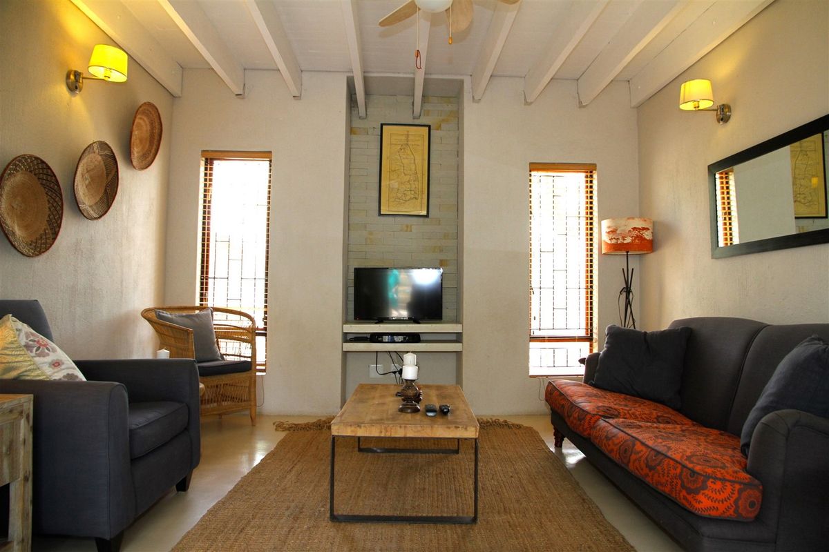A cozy living room featuring exposed beam ceilings, a built-in fireplace alcove, and dual windows providing natural light.