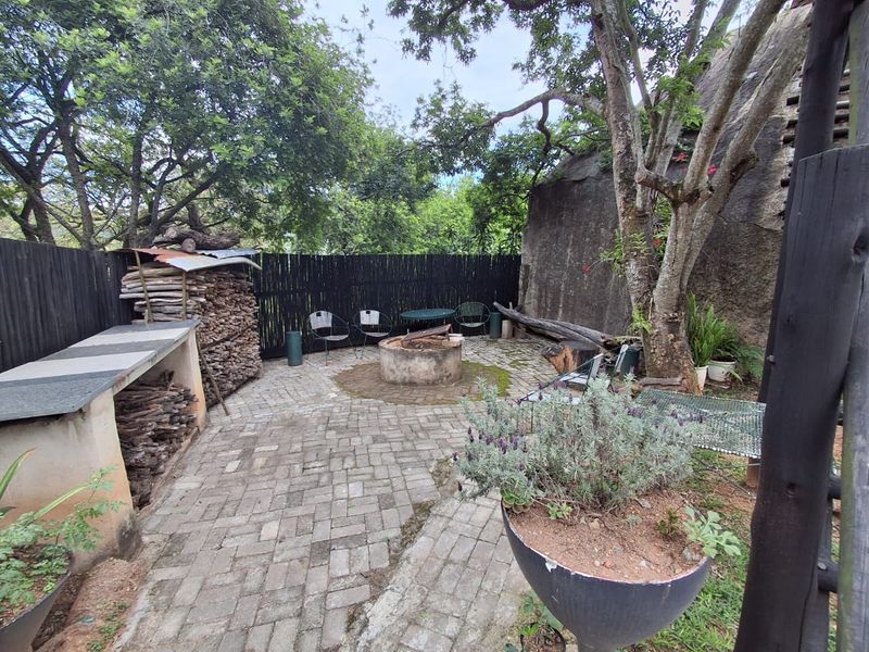 Outdoor entertainment area featuring a paved patio, built-in braai, and a rustic boma fire pit set against a natural rock backdrop.