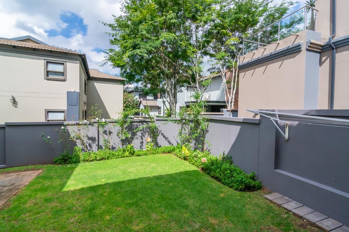 A private rear garden featuring a manicured lawn, perimeter boundary walls, and a wall-mounted retractable clothesline.