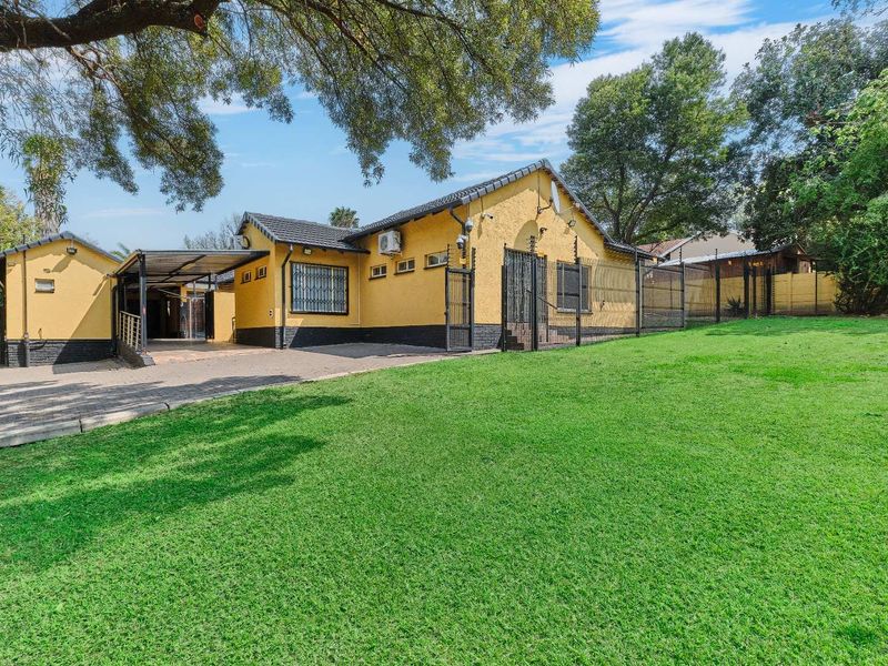 Rear view of the property featuring a paved driveway, carport, and expansive lawn area with security fencing and bars.