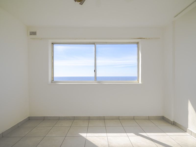 An empty bedroom featuring tiled flooring and a large sliding window with a clear ocean view.