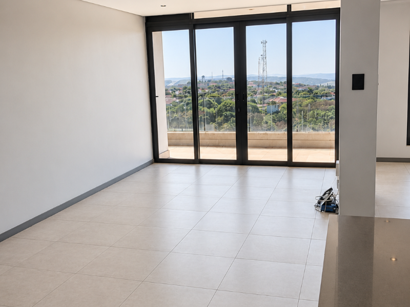 Spacious open-plan living area featuring large format floor tiles, recessed lighting, and expansive sliding glass doors leading to a balcony with scenic views.