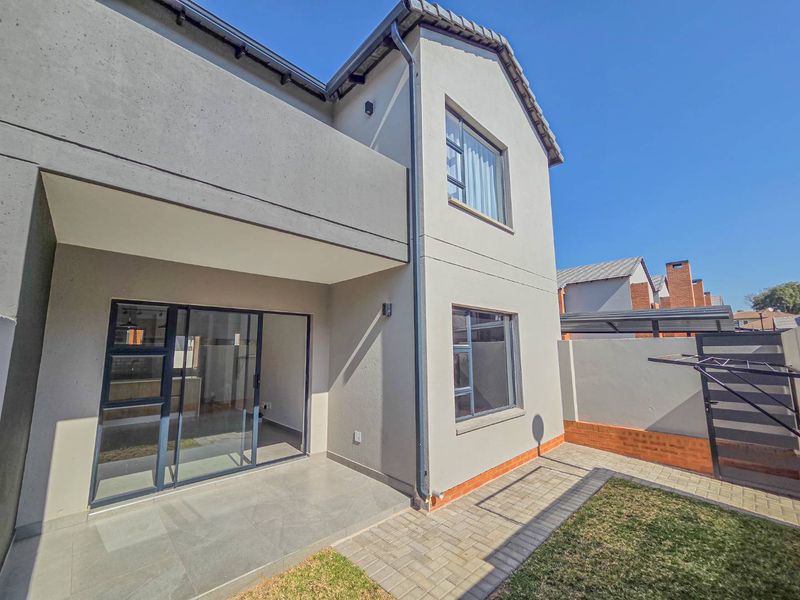 Rear view of a modern townhouse featuring a paved patio area, sliding glass doors, and a private garden space with boundary walling.