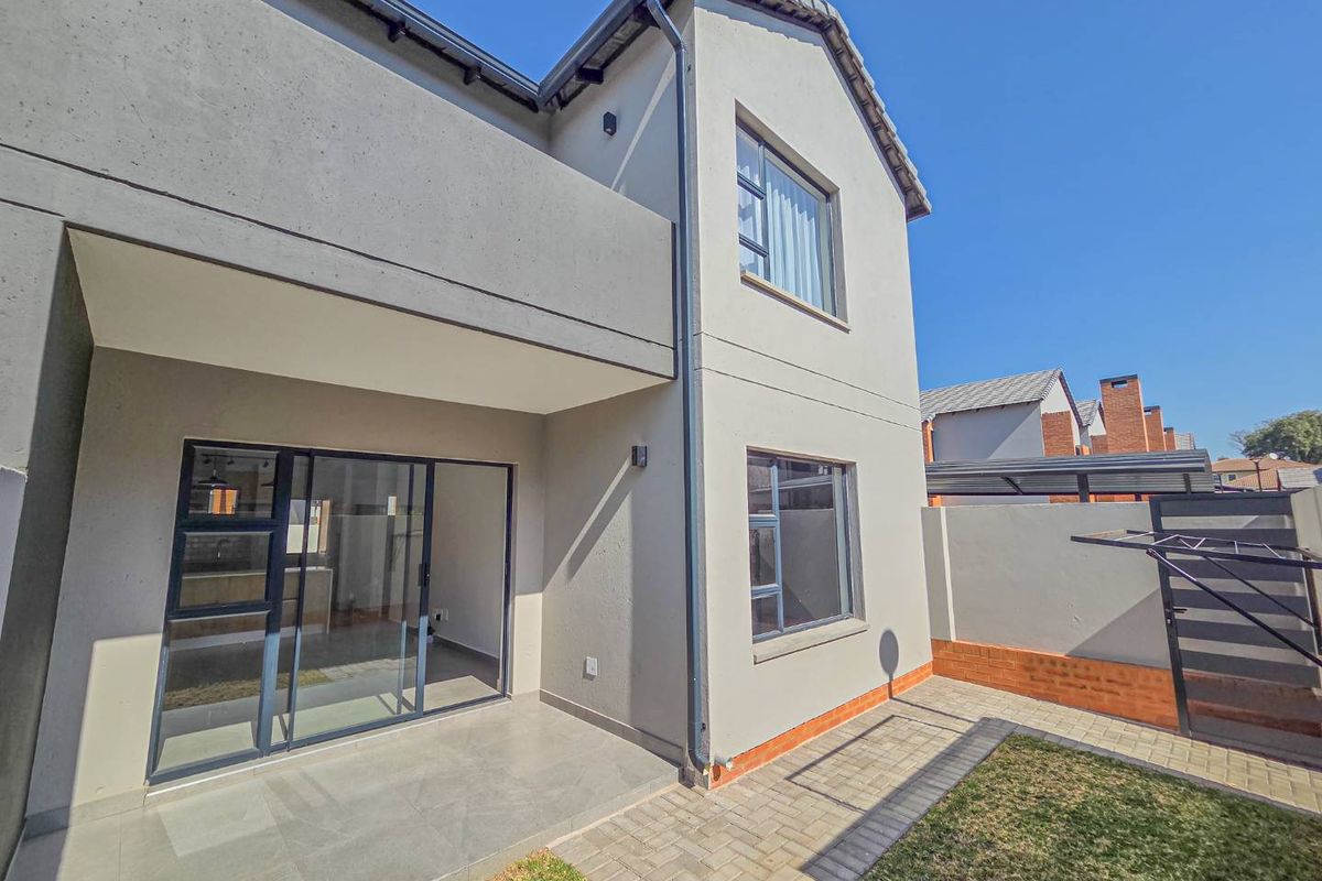 Rear view of a modern townhouse featuring a paved patio area, sliding glass doors, and a private garden space with boundary walling.