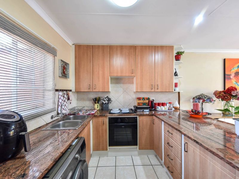 A functional kitchen featuring granite countertops, light wood-finish cabinetry, a built-in oven with hob, and tiled flooring.