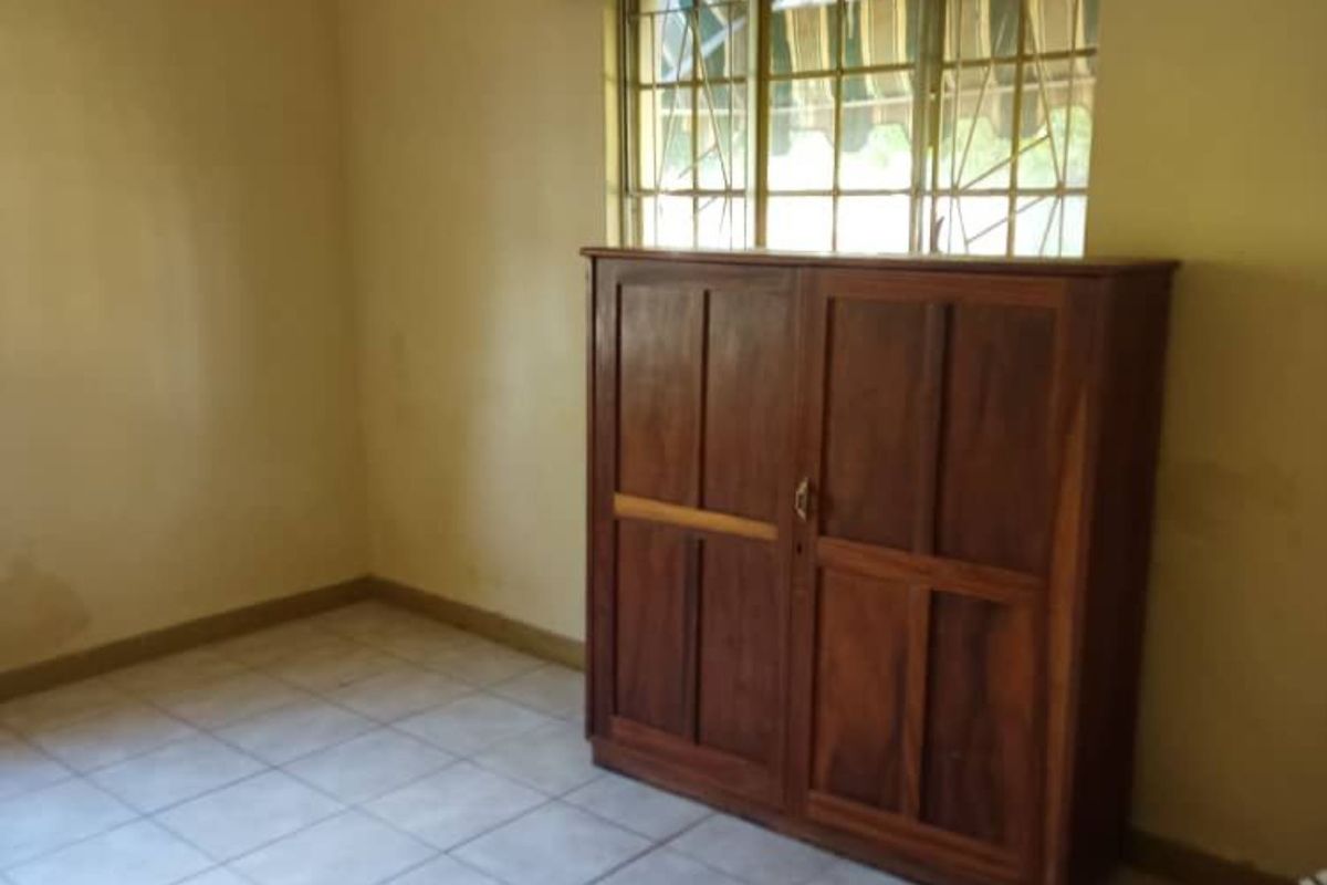 A simple bedroom featuring tiled flooring, a window with security bars, and a built-in wooden cabinet.