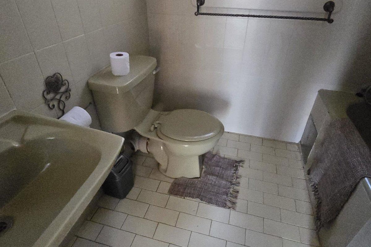 A dated bathroom featuring original colored sanitaryware, tiled flooring, and wall tiling, offering significant potential for a modern renovation.