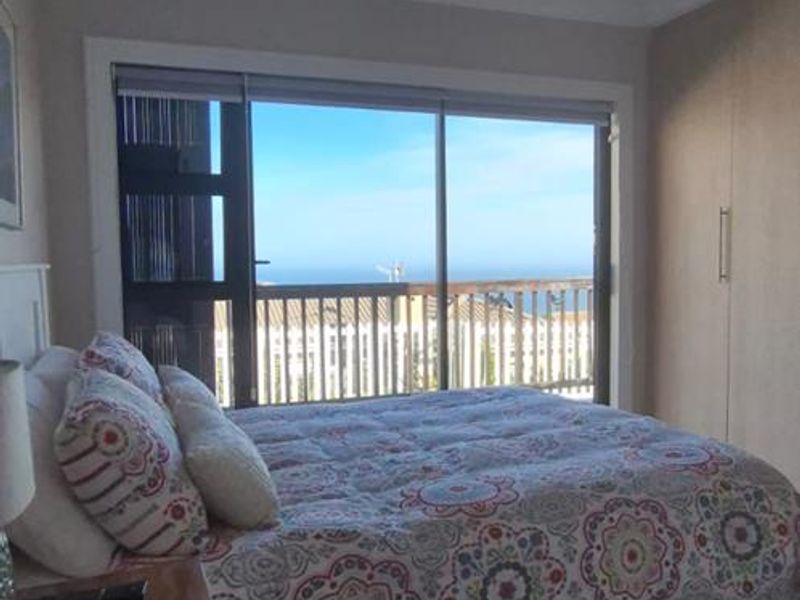 A well-lit bedroom featuring built-in cupboards, laminate flooring, and a sliding glass door that opens to a balcony with ocean views.
