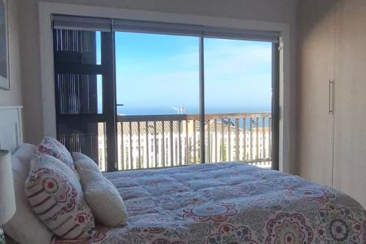 A well-lit bedroom featuring built-in cupboards, laminate flooring, and a sliding glass door that opens to a balcony with ocean views.
