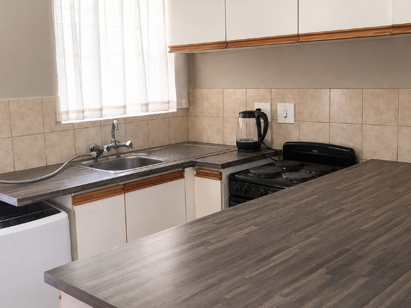 Functional kitchen featuring white cabinetry, dark laminate countertops, tiled backsplash, and a built-in electric stove with a breakfast bar extension.