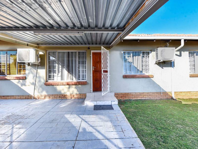 Rear exterior view of the townhouse featuring a covered paved patio, lawn area, and wall-mounted air conditioning units.