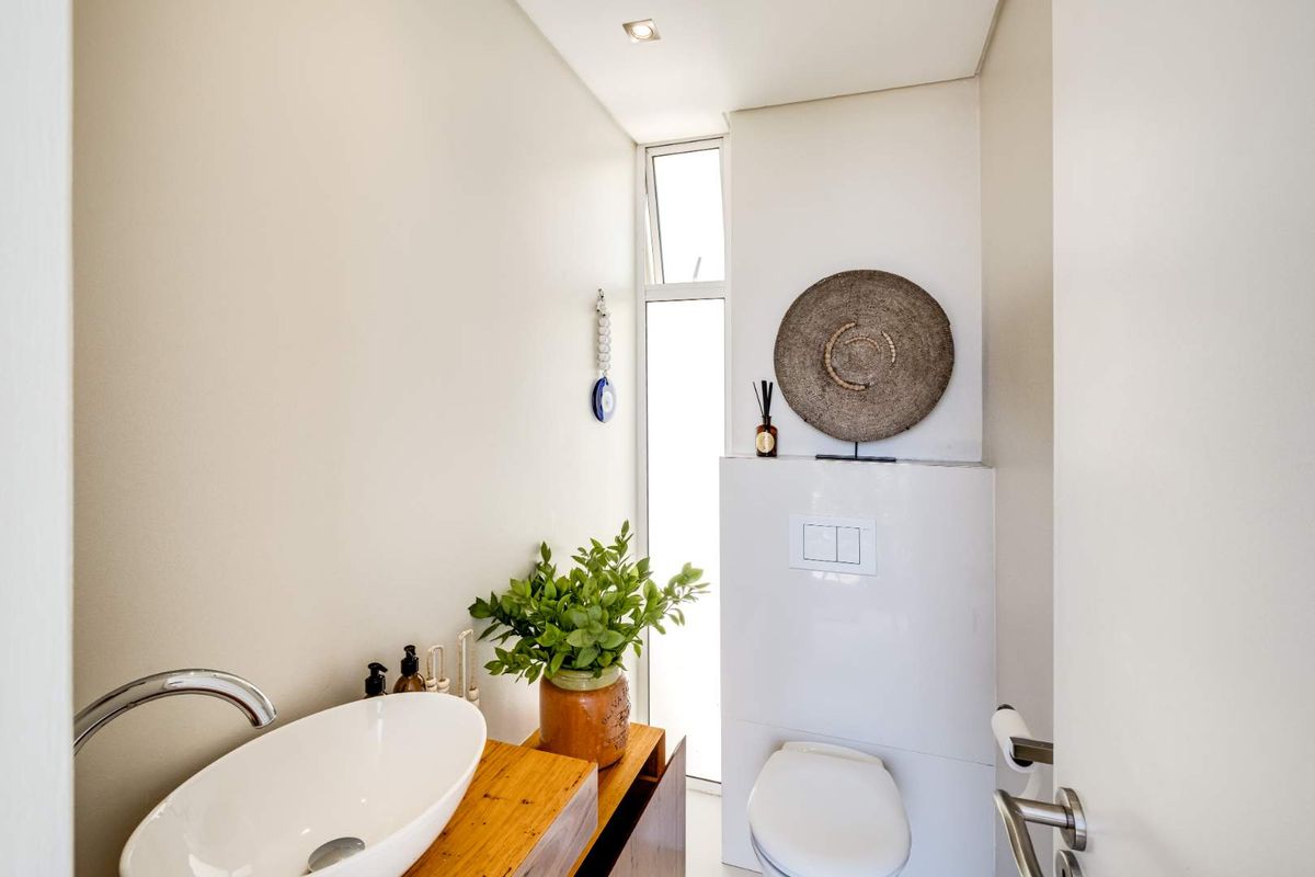 A modern guest bathroom featuring a sleek vessel sink on a wooden vanity and a wall-mounted toilet with a concealed cistern.