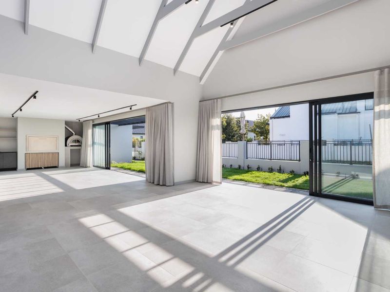 Spacious open-plan living area featuring vaulted ceilings, exposed rafters, large format floor tiles, and seamless indoor-outdoor flow through expansive sliding glass doors.
