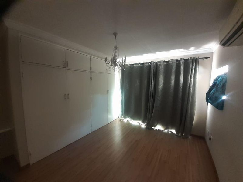 A spacious bedroom featuring extensive built-in cupboards, laminate flooring, and a wall-mounted air conditioning unit.