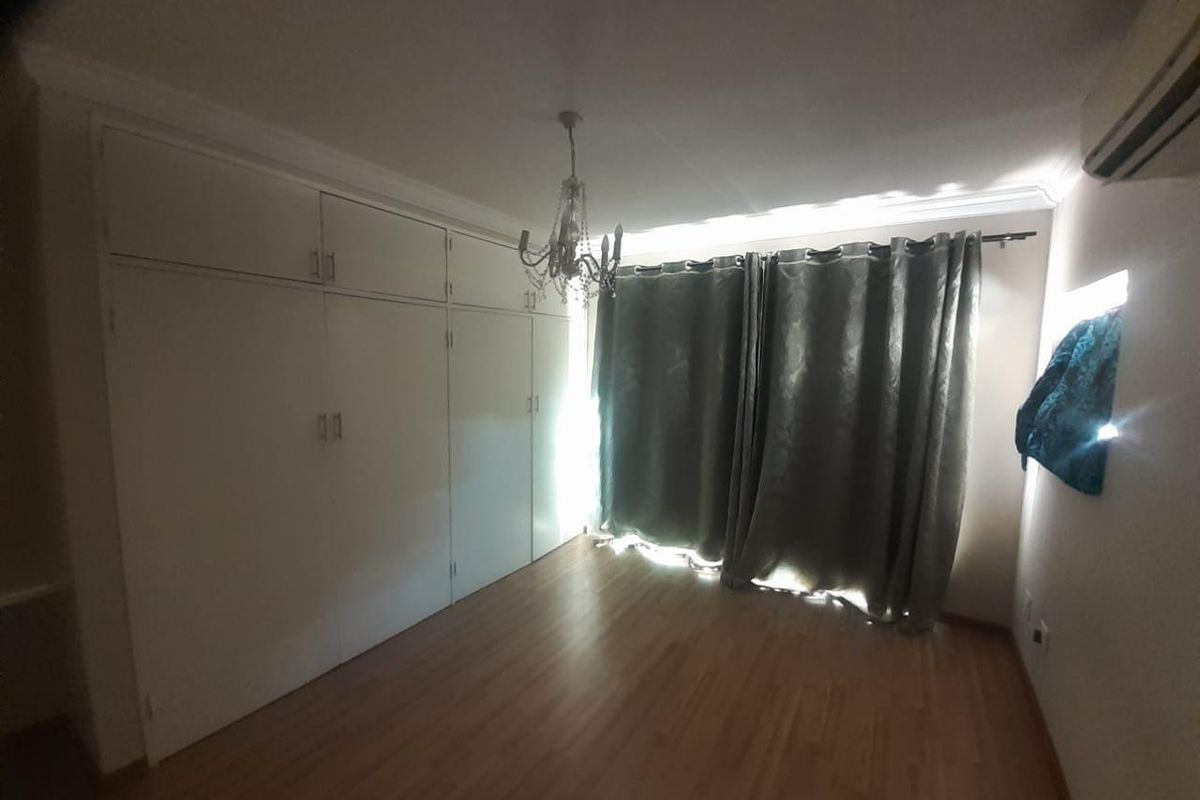 A spacious bedroom featuring extensive built-in cupboards, laminate flooring, and a wall-mounted air conditioning unit.