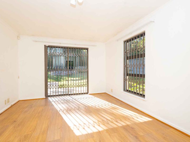 An empty, sunlit living room featuring laminate flooring, a sliding glass door with security gate, and window security bars.