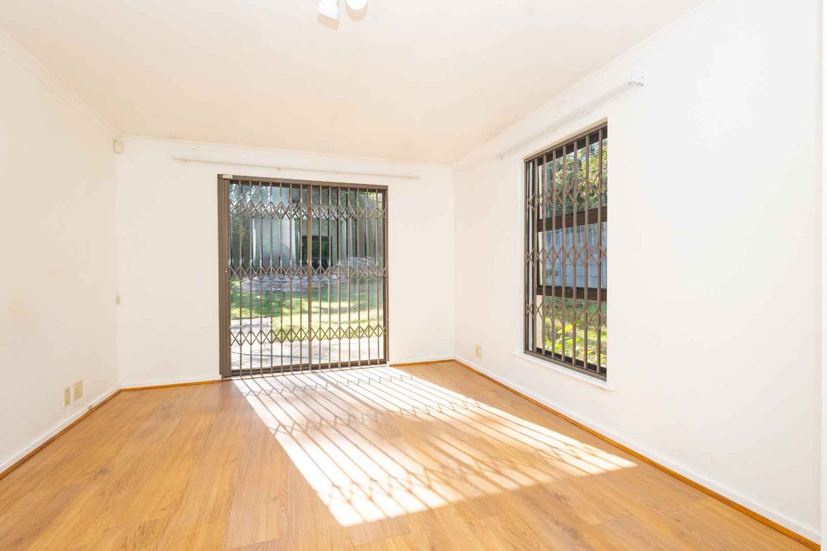 An empty, sunlit living room featuring laminate flooring, a sliding glass door with security gate, and window security bars.
